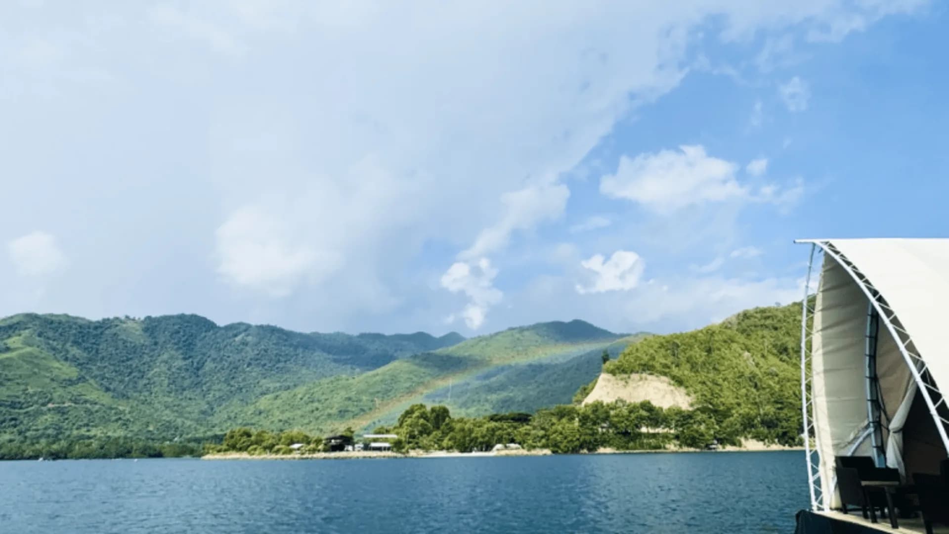 A rainbow over forested hills across the water, seen from the deck of a Reef Resort glamping tent